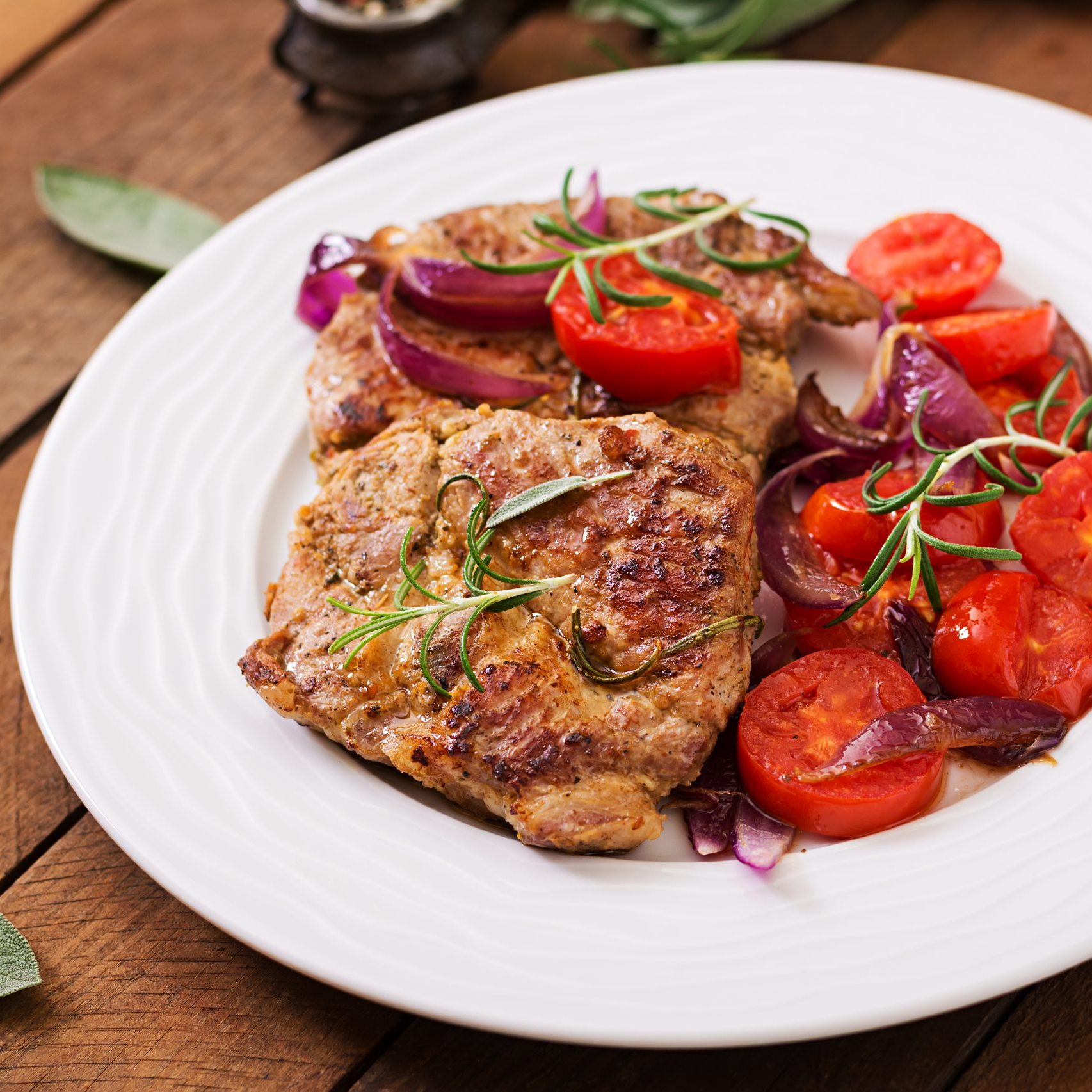 Juicy pork steak with rosemary and tomatoes on a white plate